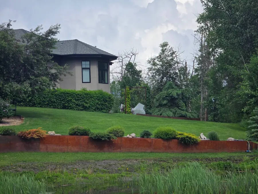 Corten steel retaining wall terracing a landscaped slope above a pond