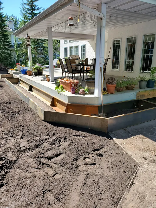 Newly fabricated Corten steel garden beds wrapping a raised patio in a custom backyard install
