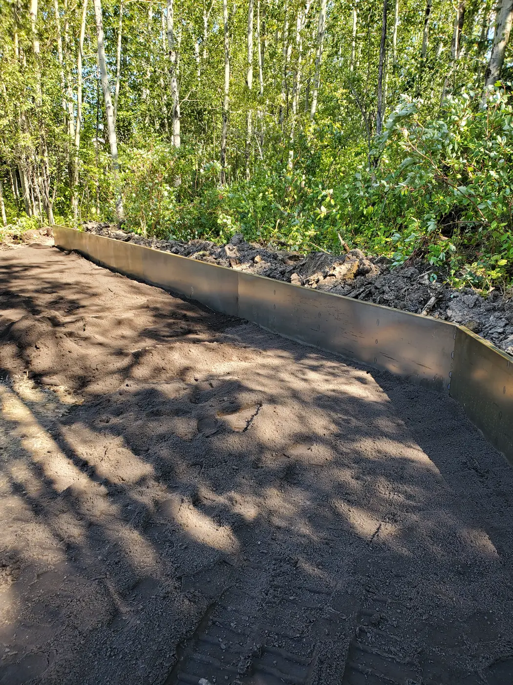 Low Corten steel retaining edge running along a graded woodland path