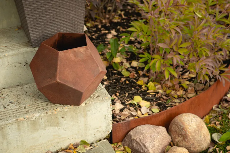 Faceted Corten steel planter on a concrete step beside Corten garden edging