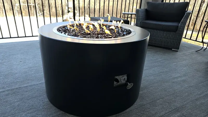 Custom powder-coated steel fire table with stainless burner ring and black fire glass on a covered deck