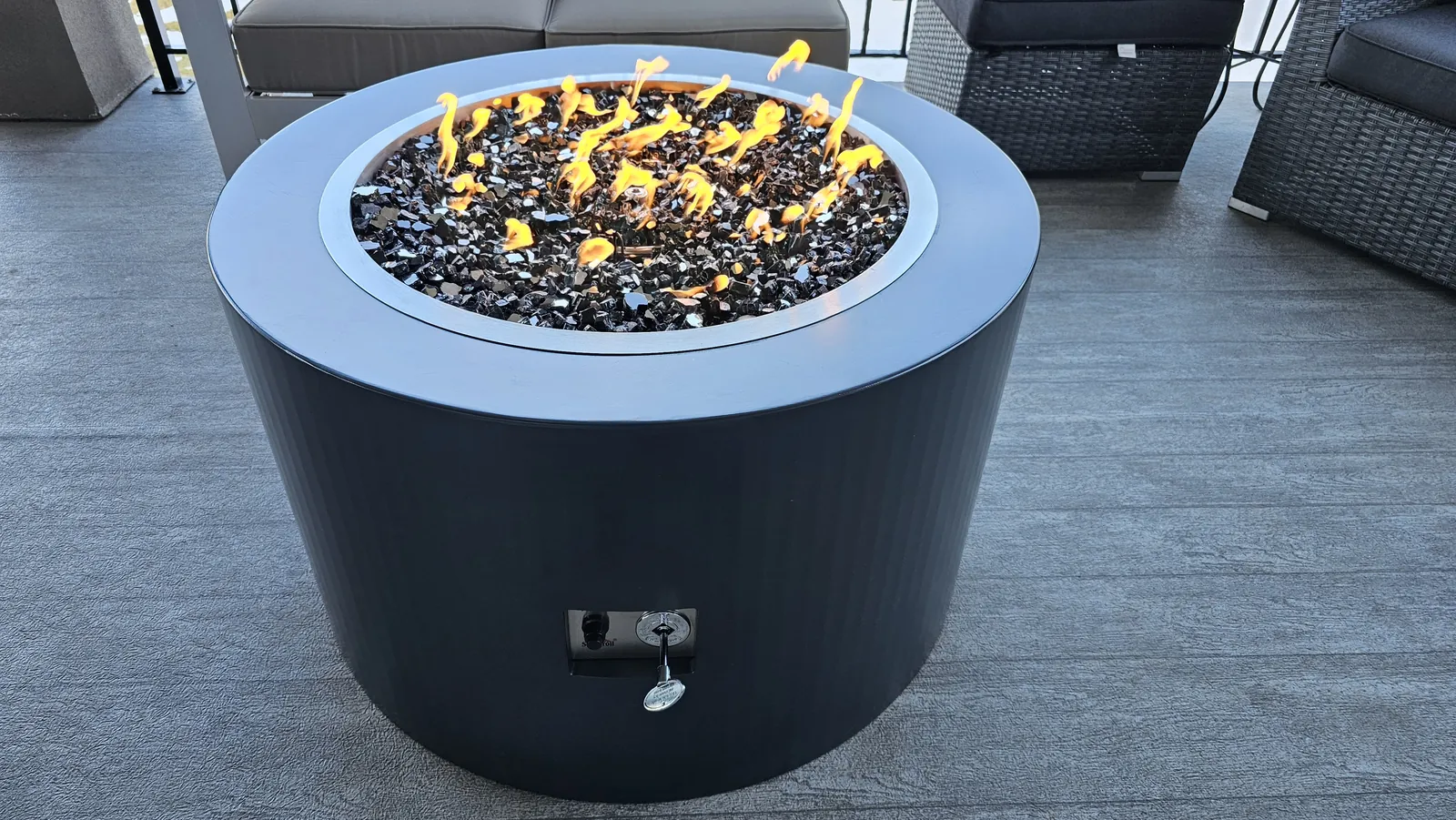 Round steel fire table with lit flames and black fire glass at dusk