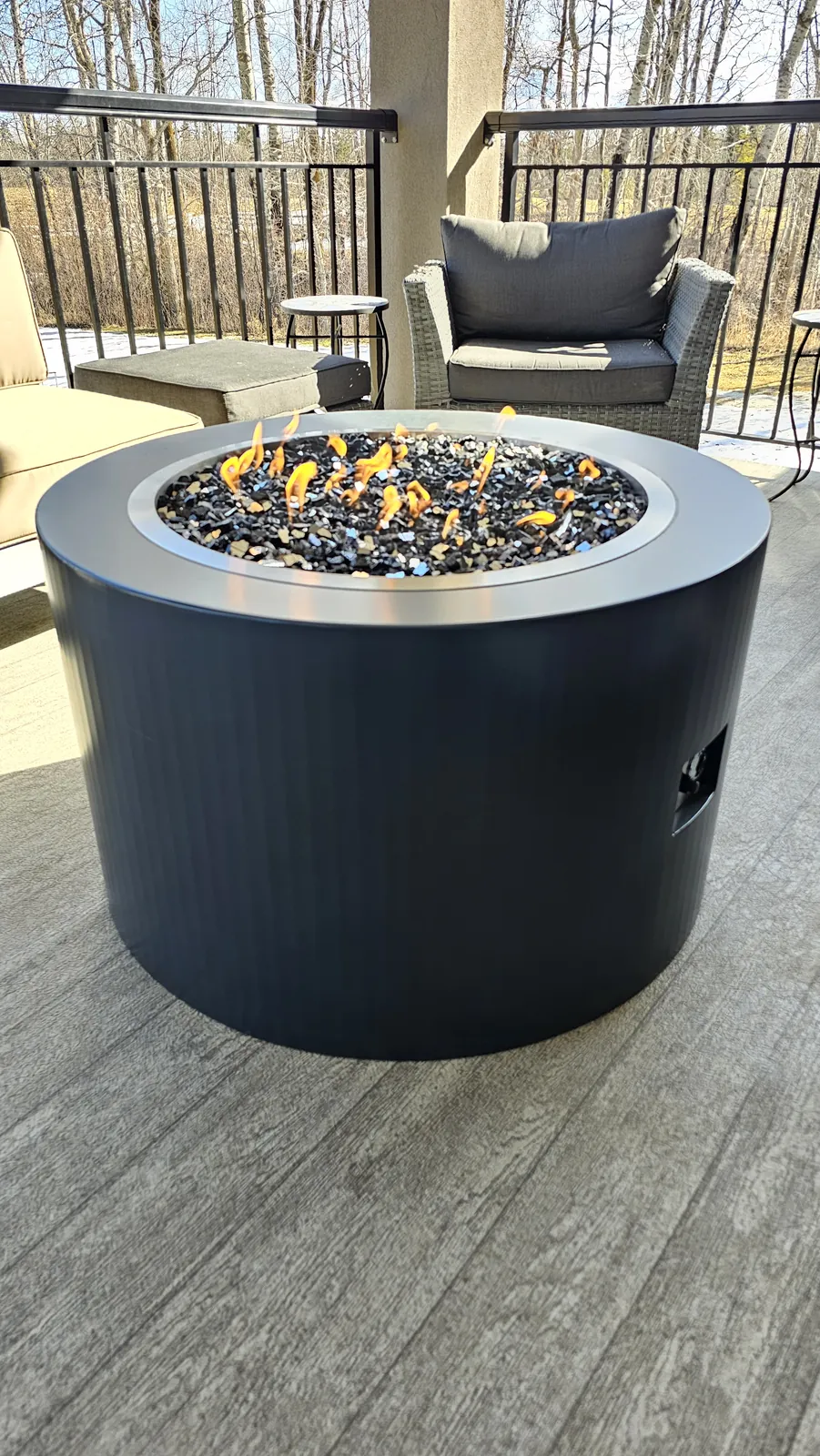 Powder-coated steel fire table on a back deck overlooking a wooded yard
