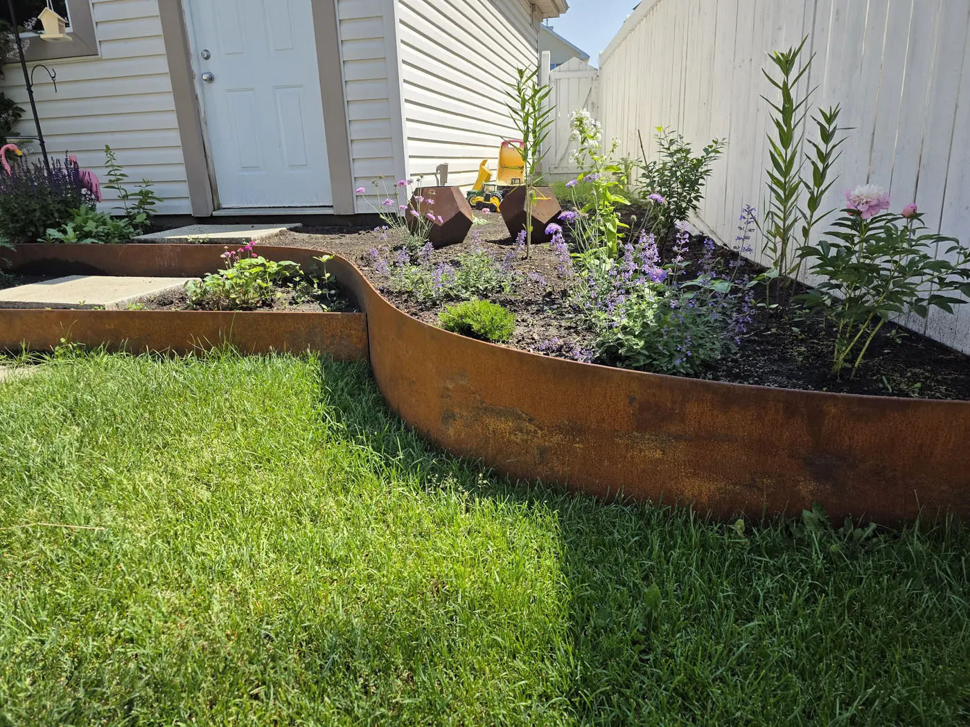 Weathered Corten steel edging defining a flowering garden bed with faceted Corten planters