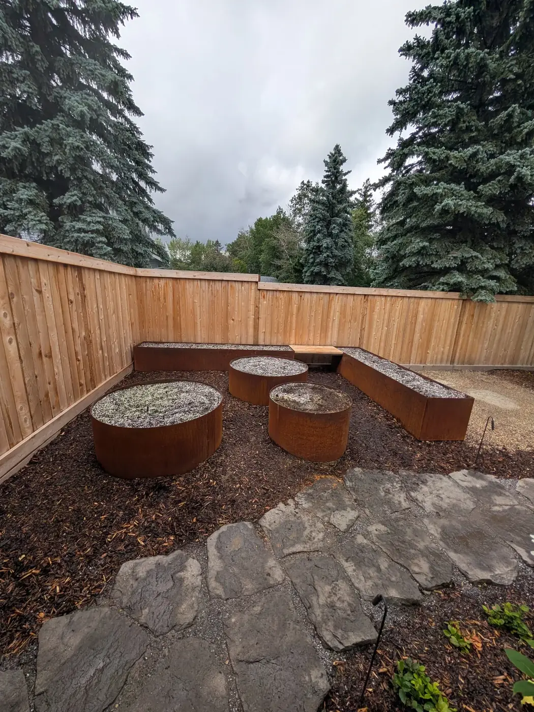 Circular and rectangular Corten planters with cedar bench along a flagstone patio