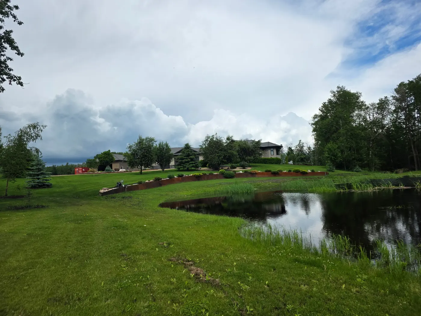 Long curved Corten steel retaining wall along a sloped acreage lawn beside a pond