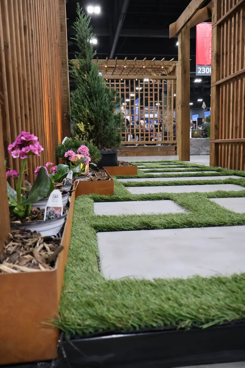 Overview of the Staaltec show booth with Corten planters, water feature, and fire table