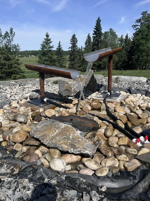 Custom Corten steel water feature with twin spill troughs cascading into a river-rock basin