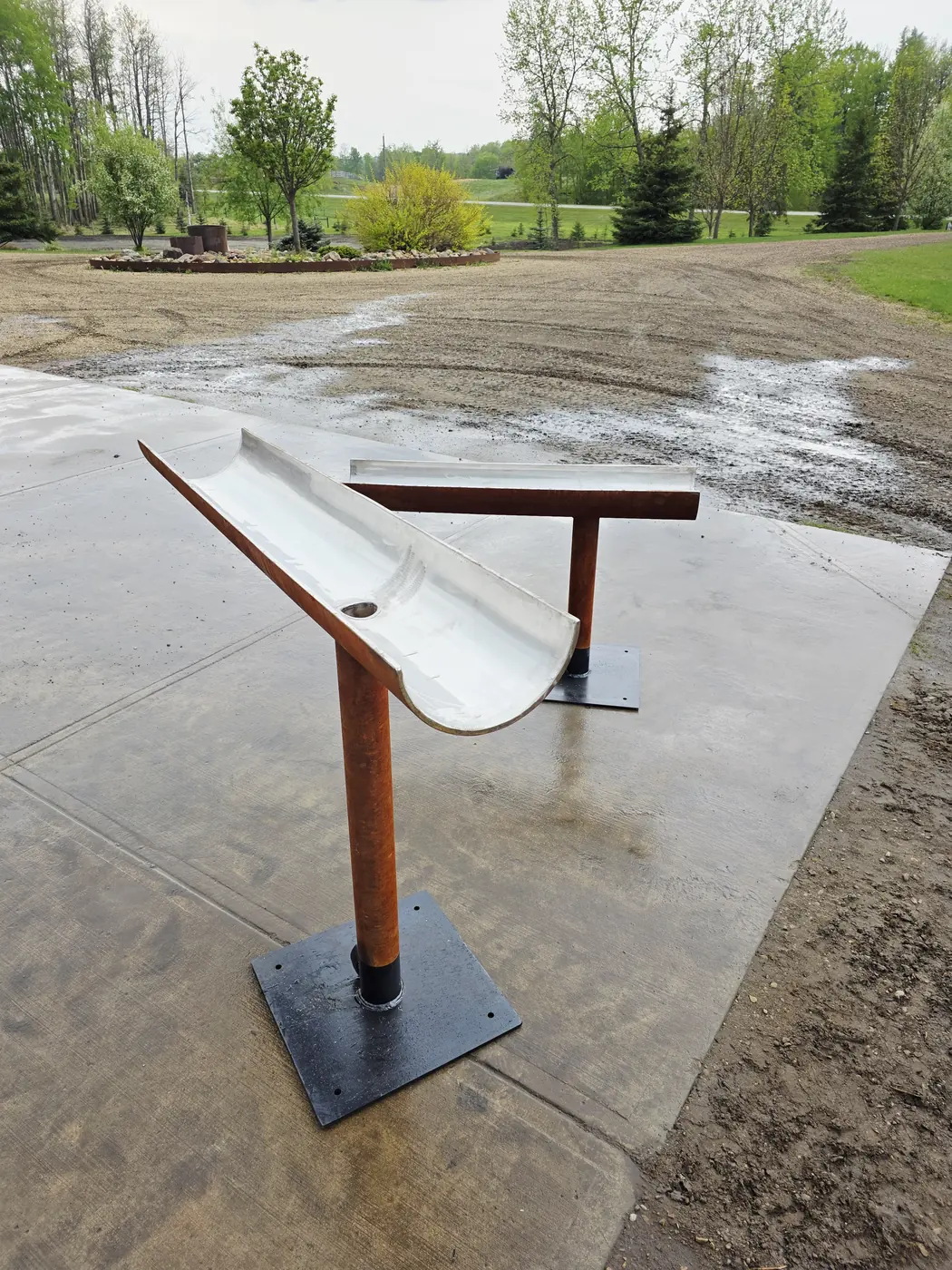 Twin Corten steel spill-trough spouts mounted on base plates before installation